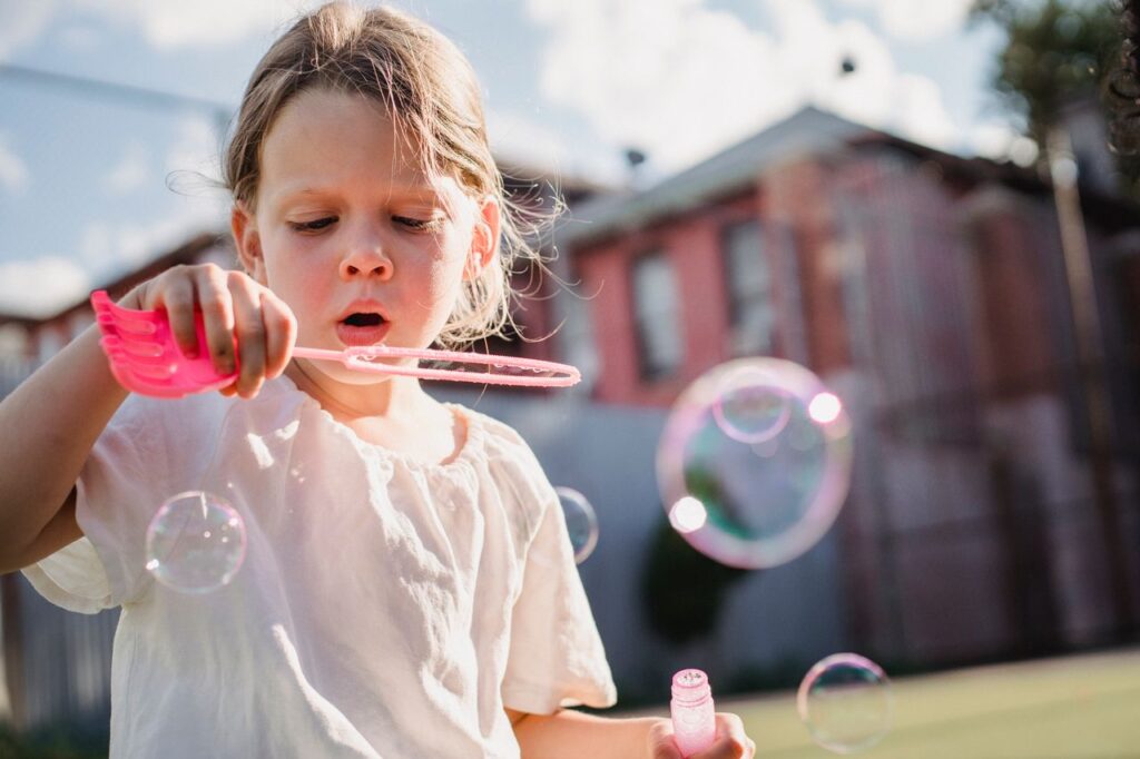 A young girl joyfully plays with bubbles outdoors on a sunny day.