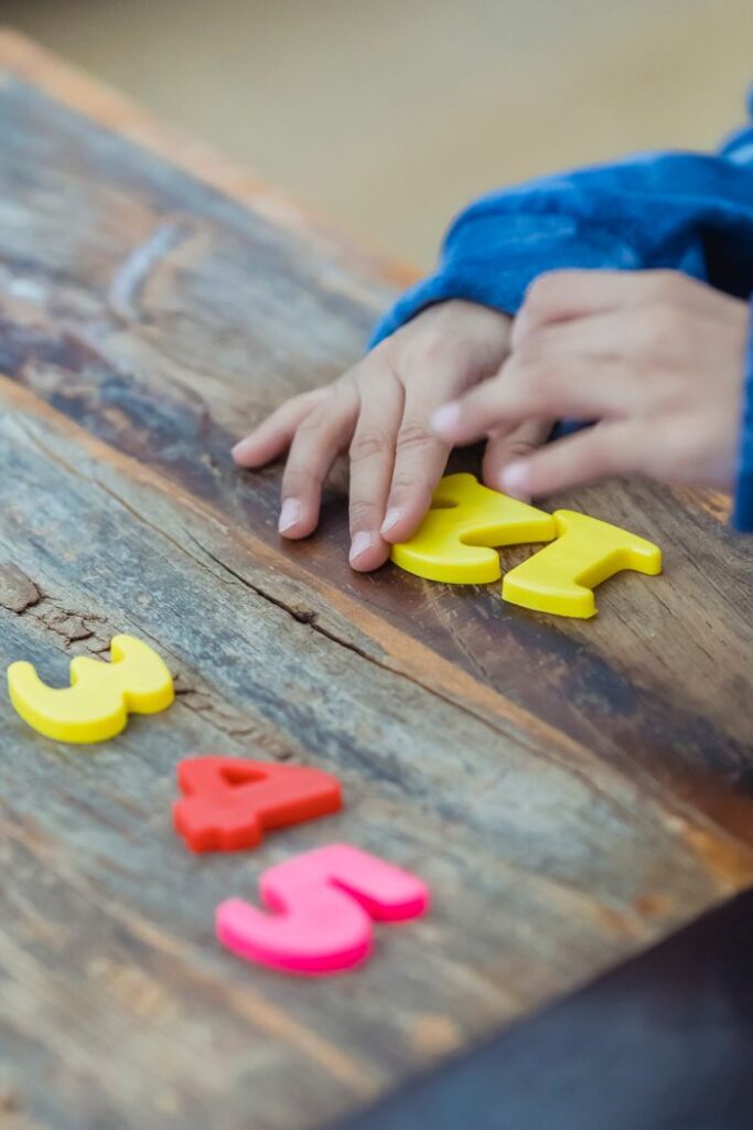 From above of crop anonymous kid counting colorful numbers placed on wooden table